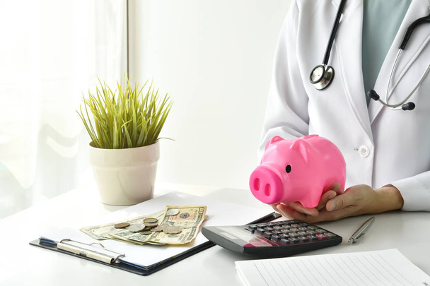 Концепція медичного та медичного страхування, Доктор, який тримає скарбничку та гроші на лікарняному фоні, Економія грошей на медичні витрати
. - Фото, зображення