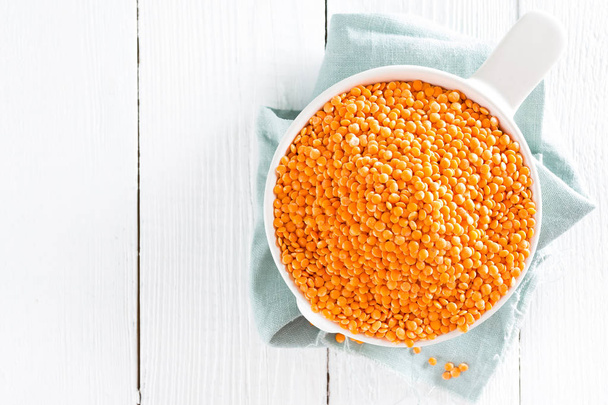 Raw lentil in bowl on table. Fresh lentils. Vegetarian food. White wooden background. Top view  - 写真・画像