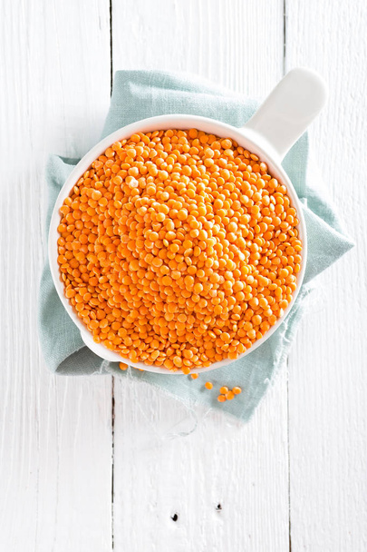 Raw lentil in bowl on table. Fresh lentils. Vegetarian food. White wooden background. Top view  - 写真・画像