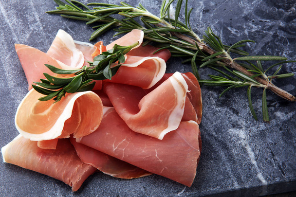 Italian prosciutto crudo or jamon with rosemary. Raw ham on wood - Foto, imagen