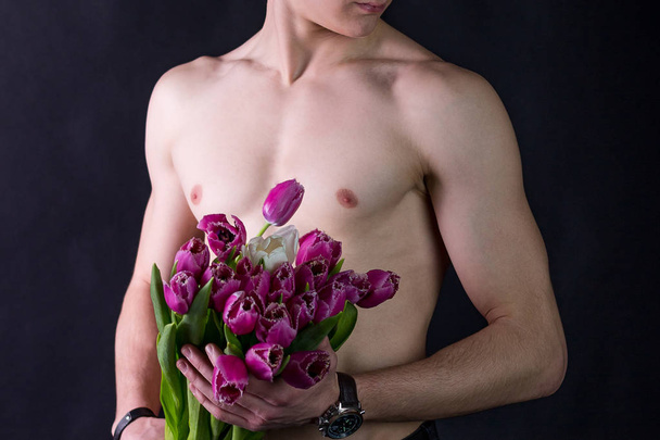 a young guy with a beautiful, naked torso holding a large bouquet of purple tulips and one white tulip, a bouquet for a loved ones holiday. - Photo, image