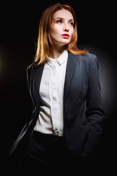 Portrait d'une fille sexy aux cheveux roux sur fond noir. Belle femme d'affaires en costume et chemise
. - Photo, image