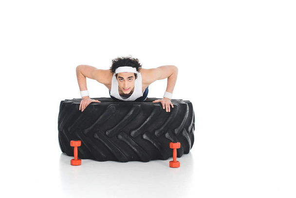 Young thin sportsman doing push ups on tire of wheel isolated on white - Photo, Image