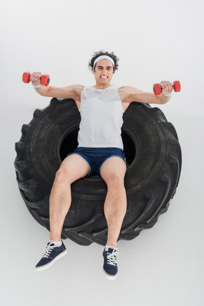 High angle view of thin sportsman exercising with dumbbells inside tire of wheel isolated on white - Φωτογραφία, εικόνα