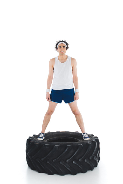 Fiatal vékony sportember, állva a gumi kerék elszigetelt fehér - Fotó, kép