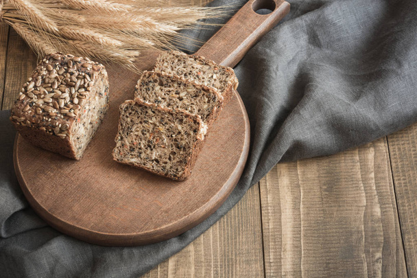 Loaf of fitness rye bread with ears of wheat, sliced on cutting board. Close up. Copy space. - Foto, Bild