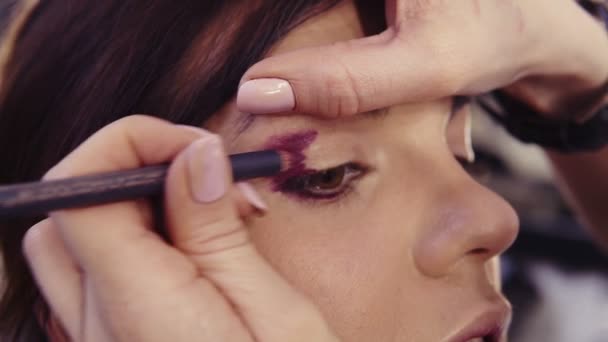 Applying purple eyeliner in the outer corner and outer crease to create a flawless smokey eyes look. Brunette caucasian looking girl with hazelnut eyes. - Felvétel, videó