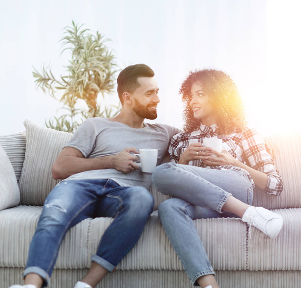 Beautiful couple holding a cup of drink while sitting on the couch at home - Foto, immagini