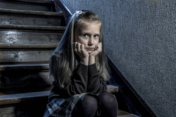 Niña de 7 u 8 años triste deprimida y preocupada sentada en la escalera desesperada y asustada sufriendo acoso escolar
  - Foto, Imagen