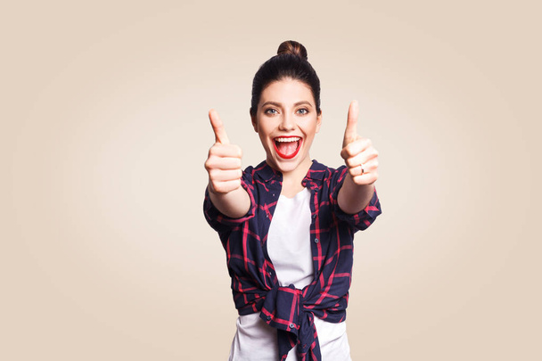 young happy woman with casual style showing thumbs up on beige background  - 写真・画像