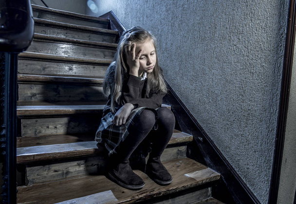 7 or 8 years old sad depressed and worried schoolgirl sitting on staircase desperate and scared suffering bullying and harassment at school  - Foto, Imagen
