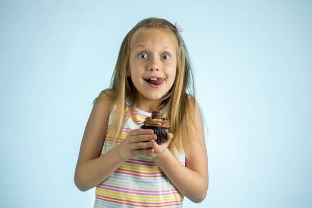 young beautiful happy and excited blond girl 8 or 9 years old holding chocolate cake on her hand looking spastic and cheerful in sugar addiction concept - 写真・画像