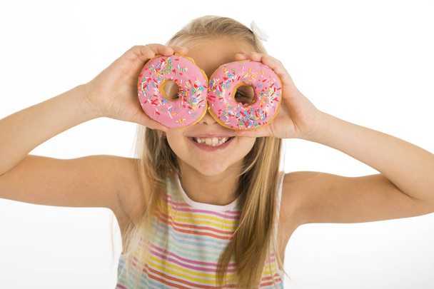joven hermosa chica rubia feliz y emocionada 8 o 9 años de edad sosteniendo dos donuts en sus ojos mirándolos a través de ellos jugando alegre
  - Foto, Imagen