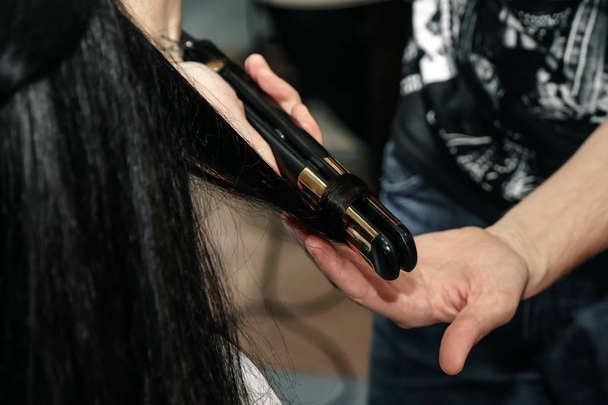 Close up of stylist hands with styling iron straightening woman hair at salon - Φωτογραφία, εικόνα