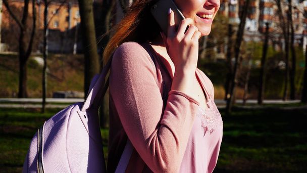 Estudiante alegre caminando en el parque y hablando por teléfono inteligente
. - Foto, imagen