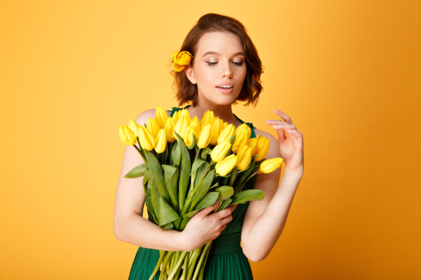 retrato de mujer joven mirando ramo de tulipanes amarillos en mano aislados en naranja
 - Foto, Imagen