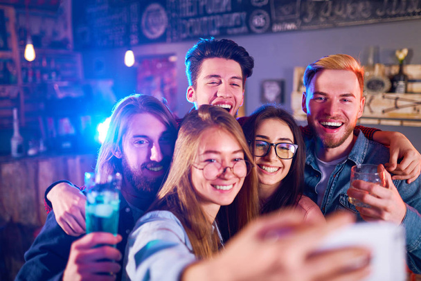 Selfie Time. Young Group of Friends Partying In A Nightclub And Toasting Drinks. Happy Young People With Cocktails At Pub. The People Have A Great Mood And They Smile A Lot - Foto, imagen