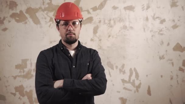 Hombre adulto seguro en casco de construcción roja y gafas está mirando en la cámara
 - Imágenes, Vídeo