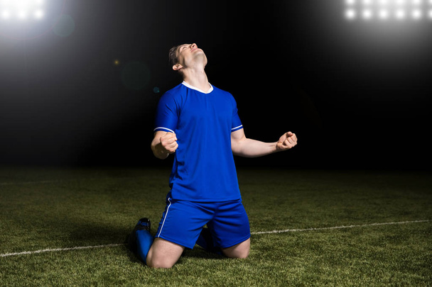 Voetballer knieën glijden op het gras in een stadion een overwinning vieren - Foto, afbeelding