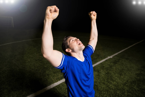 Vrolijke mannelijke voetballer verhogen van zijn armen en viert zijn overwinning in het stadion - Foto, afbeelding