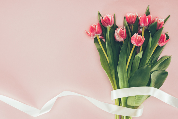 bouquet of beautiful pink tulips with green leaves and ribbon on pink  - Foto, imagen