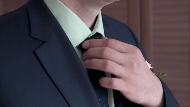 Porträt eines Geschäftsmannes, der seine Krawatte im Amt anpasst. Clip. Mann im schwarzen Anzug und weißem Hemd richtet seine Krawatte mit den Händen, eine Nahaufnahme ohne Gesicht - Foto, Bild