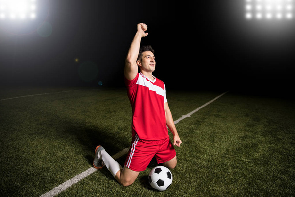 Feliz joven jugador de fútbol con tobogán de rodilla celebrando un gol durante un partido de Copa del Mundo
 - Foto, Imagen
