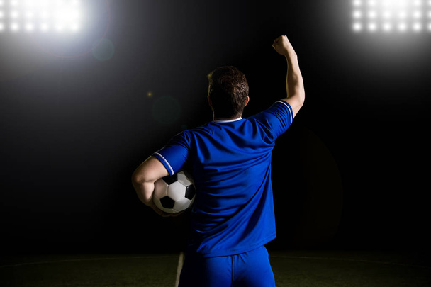Mannelijk voetbalspeler bezit is van een voetbal zijn arm verhogen en vieren na het scoren van een goal in het stadion - Foto, afbeelding