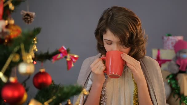 Pretty little girl standing near Christmas tree and drinking cappuccino, holiday - Footage, Video