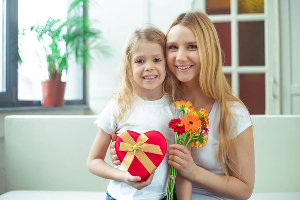 Όμορφη χαρούμενη μητέρα και μια μικρή κόρη χαμογελώντας αγκαλιάσει με δώρα στα χέρια τους και κοιτάξτε στην κάμερα. Γενέθλια. 8 Μαρτίου. Ημέρα της γυναίκας. - Φωτογραφία, εικόνα