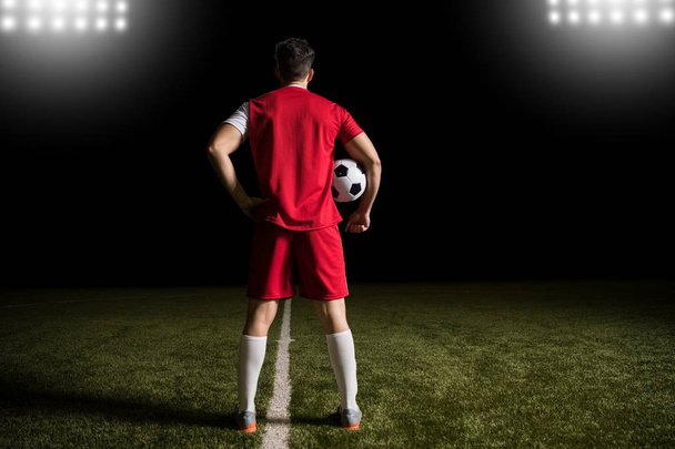 Volledige lengte van voetballer die permanent in de rode trui op voetbalveld met bal - Foto, afbeelding