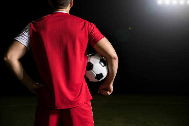 Vue arrière du sportif en maillot rouge debout dans le stade avec une balle sous le bras
 - Photo, image