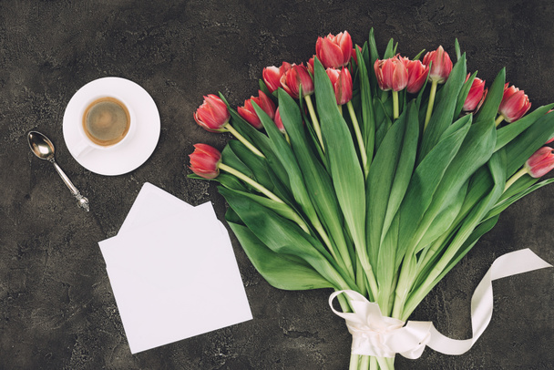 top view of beautiful red tulips, cup of coffee and blank envelope with greeting card - Φωτογραφία, εικόνα