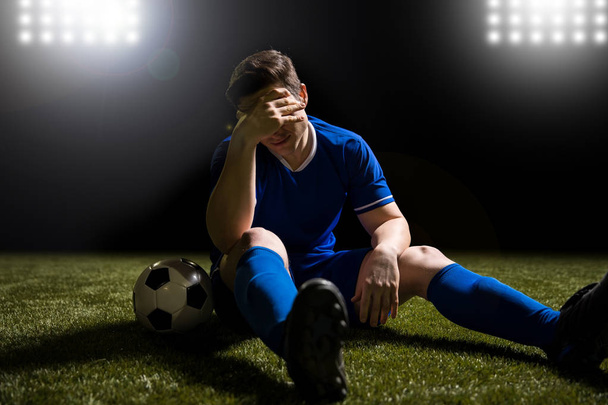 Jugador de fútbol decepcionado en azul sentado en el campo después de perder el partido
 - Foto, imagen
