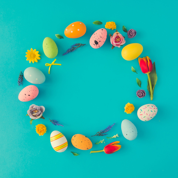 Kreatives Osterlayout in Form eines Kreiskranzes aus bunten Eiern und Blumen auf blauem Hintergrund  - Foto, Bild
