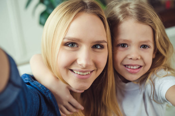 Smiling and happy mom and daughter are hugging each other at home on the couch. Mom and daughter  have fun.  - Φωτογραφία, εικόνα