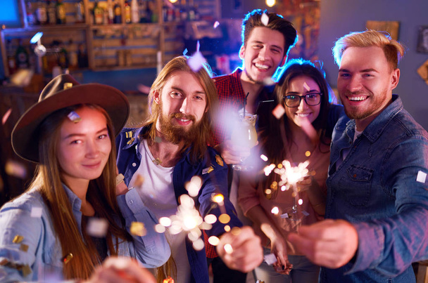 Young Group of Friends Partying In A Nightclub And Toasting Drinks. Happy Young People With Sparklers At Pub. The People Have A Great Mood And They Smile A Lot. - Foto, Imagem