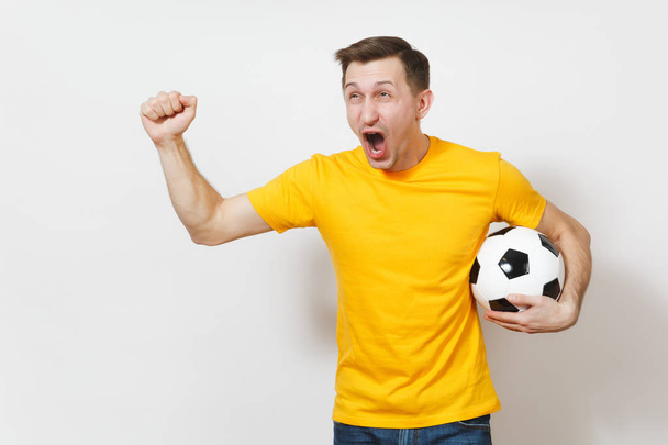 Вдохновлённый молодой европеец, фанат или игрок в жёлтой форме держит футбольный мяч, болеет за любимую футбольную команду, выразительные жестикулирующие руки изолированы на белом фоне. Концепция образа жизни. Копирование пространства
. - Фото, изображение