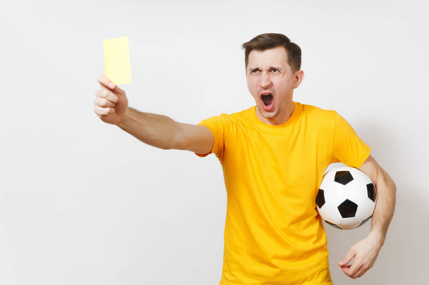 深刻な深刻な欧州青年、サッカーの審判または黄色い制服黄色のカードを示す、白い背景で隔離のサッカー ボールを保持しているプレーヤー。スポーツ、サッカー、健康的なライフ スタイルのコンセプト. - 写真・画像