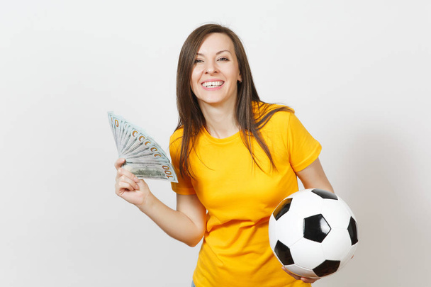 Ευρωπαϊκό νέων διασκέδαση γυναίκα, ποδόσφαιρο ανεμιστήρα ή παίκτη σε κίτρινο ομοιόμορφη εκμετάλλευση μάτσο χρήματα τραπεζογραμματίων, μπάλα ποδοσφαίρου που απομονώνονται σε λευκό φόντο. Αθλητισμός, ποδόσφαιρο παιχνίδι, ενθουσιασμό lifestyle έννοια. - Φωτογραφία, εικόνα