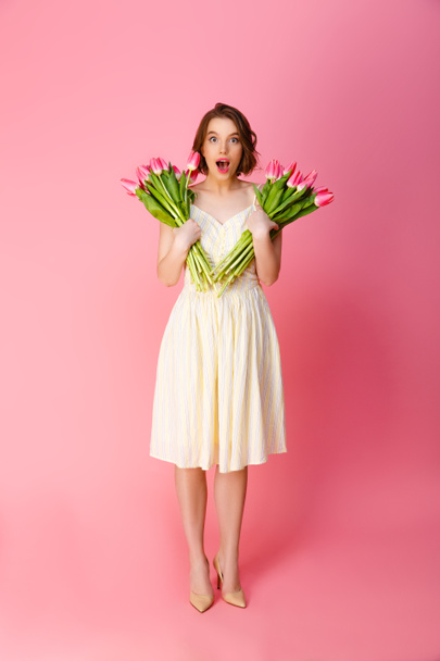 Młoda kobieta wstrząśnięty z bukiety kwiatów wiosna na różowym tle - Zdjęcie, obraz