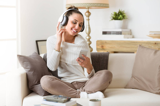 Woman listening music in headphones on a couch - Foto, Imagen