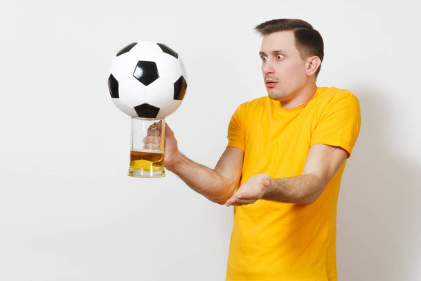 Грустные расстроен молодой растерянный европейский человек, вентилятор или игрок в желтой форме держать кружку пива, футбольный мяч приветствовать любимую футбольную команду на белом фоне. Спорт, игры, концепция образа жизни
. - Фото, изображение