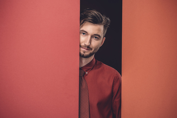 Smiling businessman behind red paper walls isolated on black - Фото, изображение