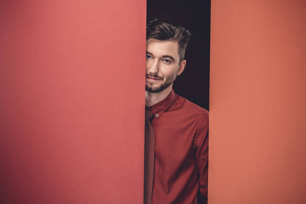Smiling young man by red paper walls isolated on black - Zdjęcie, obraz