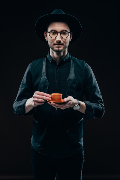 Stylish man holding cup with coffee isolated on black - Photo, Image
