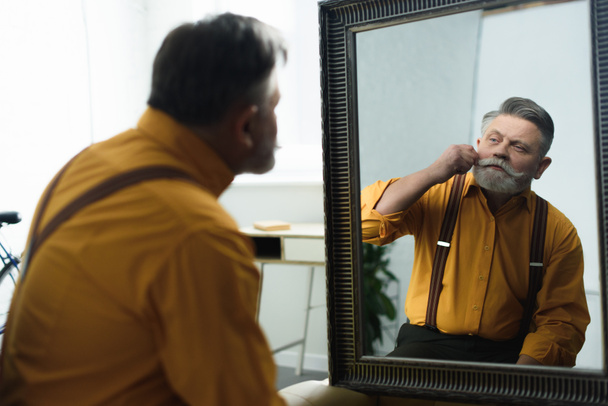 przystojny Brodaty starszy człowiek, dostosowując wąsy i patrząc w lustro - Zdjęcie, obraz
