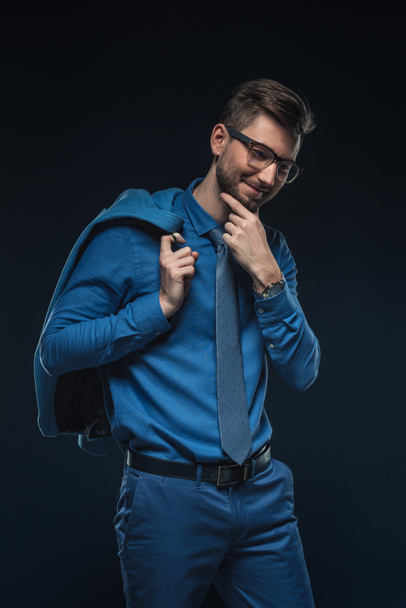 Smiling businessman in glasses holding his jacket isolated on blue - Fotó, kép