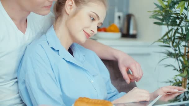 Young couple using digital tablet while having breakfast at kitchen table. - Materiał filmowy, wideo