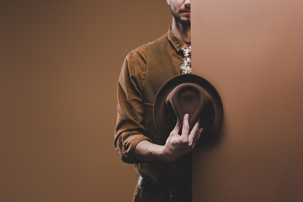Stylish man wearing coat and holding hat isolated on brown - Foto, immagini